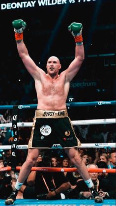 a man standing on top of a boxing ring holding his hands up in the air