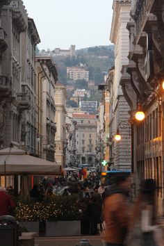 people are walking down the street in an old city with many buildings and lights on