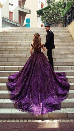 a woman in a purple dress standing next to a man on some stairs with her back turned