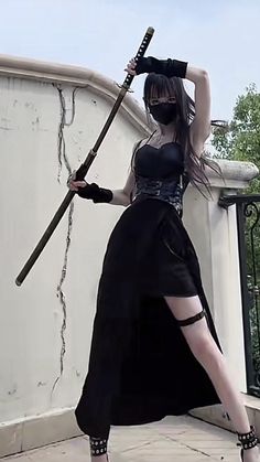 a woman dressed in black holding two swords on her head and posing for the camera