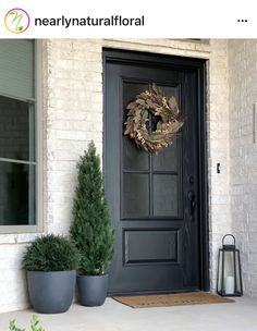 two large planters are sitting on the front porch next to a black door with a wreath