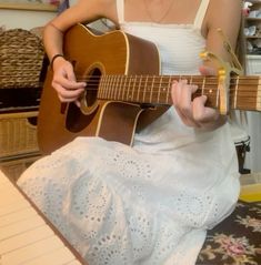 a woman is sitting on the floor playing an acoustic guitar while holding it in her hands