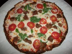 a pizza with tomatoes, meat and basil on it sitting on a white paper plate