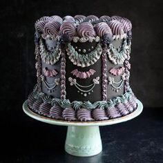 a purple and black decorated cake sitting on top of a white plate next to a dark wall