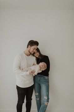 a man holding a baby while standing next to a woman with her arm around him