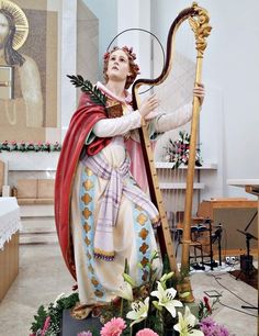 a statue of a woman holding a harp in a church with flowers around her ankles