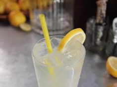 a close up of a drink on a table with lemons and glasses in the background