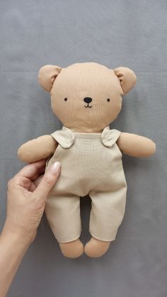 a person is holding a teddy bear in their left hand and wearing overalls on the right