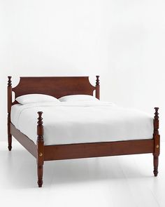 a wooden bed frame with white sheets and pillows on top of it, in front of a plain wall