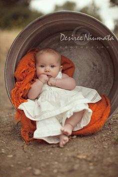 a baby is sitting in a bucket with an orange blanket on it's back