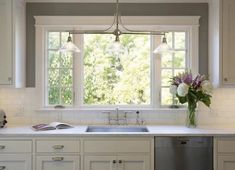 a kitchen with white cabinets and an island in front of a window that has flowers on it