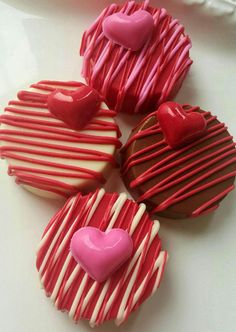 four heart shaped cookies with red and white icing on a plate next to a cupcake