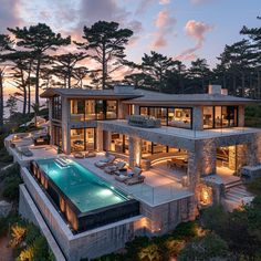 an aerial view of a house with a swimming pool and deck area at dusk, surrounded by pine trees