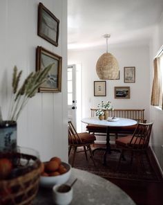 a dining room table and chairs with pictures on the wall above it, along with bowls of fruit