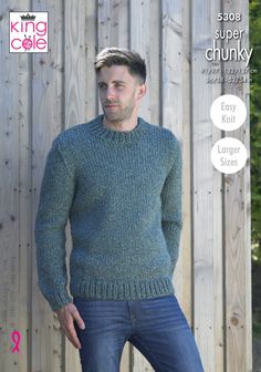 a man standing in front of a wooden fence wearing a green sweater and blue jeans