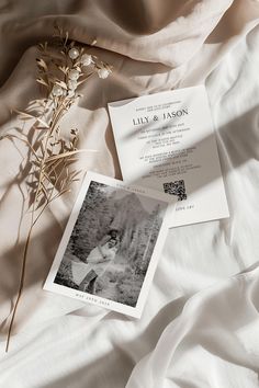 an image of a wedding card on top of a bed with white sheets and flowers