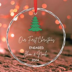 a glass ornament with a christmas tree on the front and back of it that says our first christmas engaged john & mary