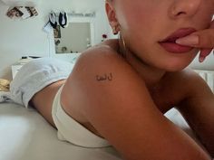 a woman laying on top of a bed with her hand under her chin and the word i love you tattooed on her chest