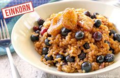 a white bowl filled with rice and blueberries on top of a table next to a fork