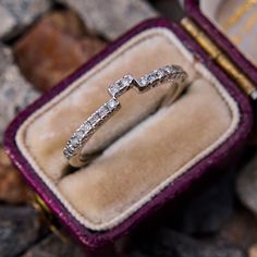 a diamond ring sits in a velvet box on some rocks and stones, with the rest of it's wedding band visible