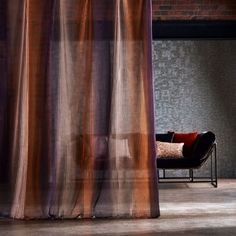 a chair sitting in front of a curtain on top of a wooden floor next to a brick wall