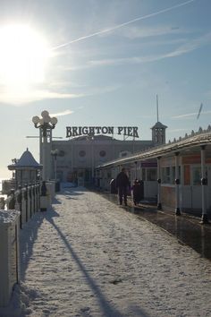 people are walking down the snow covered path to brighton pier in winter time, with bright sun shining on the building