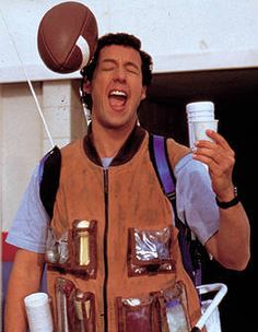 a man in an orange vest holding a water bottle and some sports balls on his head