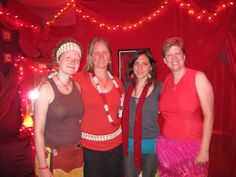 three women standing next to each other in front of a red wall with lights on it