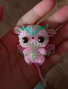 a hand holding a tiny pink and green beaded animal brooch with big eyes