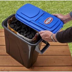 a person holding a blue cooler filled with black rocks on top of a wooden table