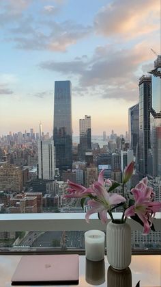 a vase with flowers on a table in front of a window overlooking a cityscape