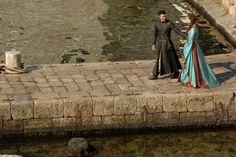 a man and woman dressed in medieval clothing standing next to water