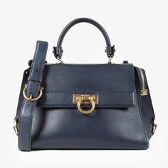 The Medium Sofia Top Handle Bag From Salvatore Ferragamo Is Expertly Crafted From Smooth Leather In Navy With Gold-Tone Hardware. Made In Italy, This Elegant Satchel Features Protective Base Studs, A Zipper Compartment At The Back, And The Signature Gancini Fastening At The Front. Its Flap Opens To A Main Zipper Compartment Lined In Matching Navy Leather And Equipped With Two Flat Pockets. This Ferragamo Bag Can Be Carried By Its Top Quilted Handle Or On The Shoulder By Its Detachable Leather Strap. Condition: Very Good; Faint Slouching, Moderate Markings On Exterior Leather, Minor Wear On Hardware, Visible Scuffings On Sides, No Inclusions Approximate Measurements: Height: 8” (20.5 Cm Ferragamo Bag, Salvatore Ferragamo Bags, Navy Leather, Handle Bag, Salvatore Ferragamo, Smooth Leather, Blue Gold, Top Handle, Sofia