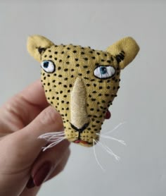 a hand holding a small stuffed animal that looks like a leopard's head with blue eyes