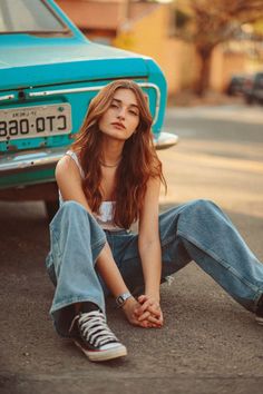 a woman sitting on the ground next to a blue car