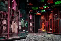 a room filled with lots of pink and green clothing hanging from the ceiling next to metal racks