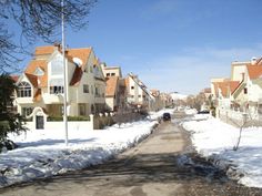 a car driving down a snow covered street next to tall white houses with red roofs