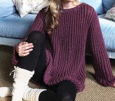 a woman sitting on the floor in front of a couch wearing a purple sweater and black leggings