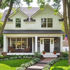 a white house surrounded by lush green trees and flowers in the front yard with an american flag hanging on the door