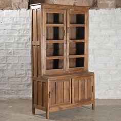 an old wooden cabinet with glass doors on the top and bottom, in front of a brick wall