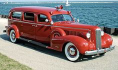 an old red firetruck is parked on the side of the road by the water