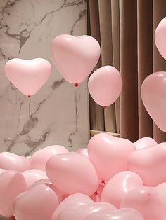 pink balloons are floating in the air near a marble wall and window with drapes