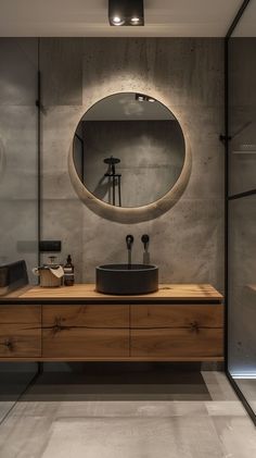 a bathroom with a large round mirror above the sink and wooden countertop, surrounded by glass walls