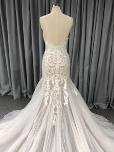 the back of a wedding dress on display in front of a gray curtained background