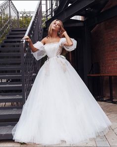 a woman in a white wedding dress is standing on the stairs with her hands behind her head