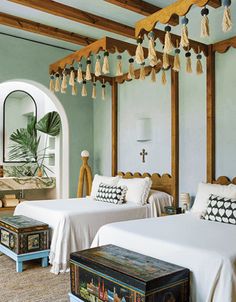 two beds in a room with blue walls and wooden beams, one has a mirror on the wall