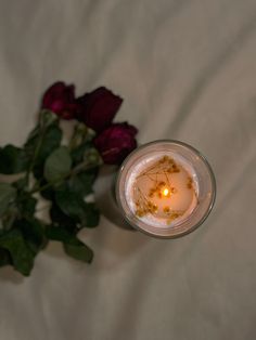 a candle with some flowers in it on a white sheet next to a red rose