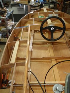 a wooden boat with steering wheel in a room full of woodworking tools and other items