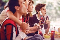 three people sitting at a table with drinks and snacks in front of them, one holding a coke bottle