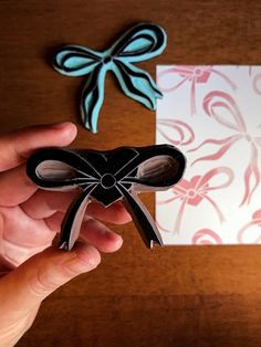 a hand holding a piece of paper with a bow on it next to a card